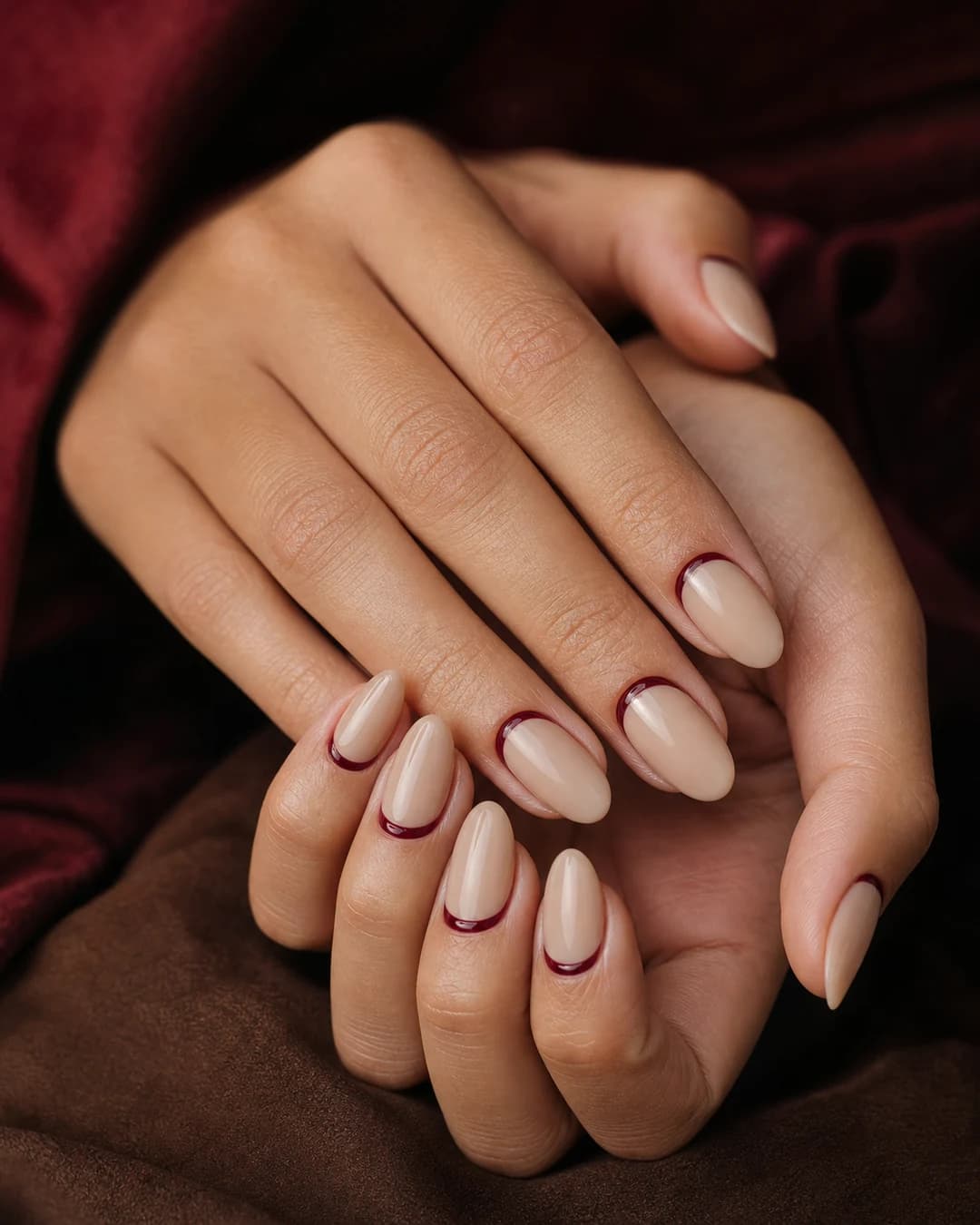 Uñas almendradas con francesa invertida burgundy oscuro en la cutícula sobre base nude piel
